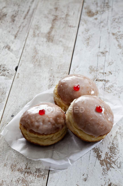 Three Bismarck doughnuts on paper on white shabby wood — Stock Photo