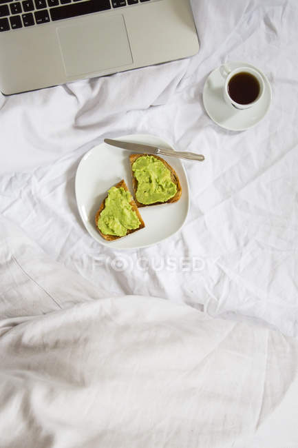 Bread with avocado cream and cup of coffee next to laptop — Stock Photo