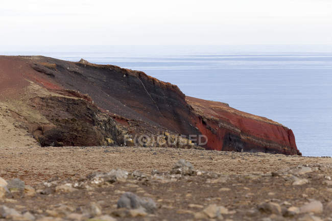 Island, haelsvik, rötliche Steilküste über Wasser — Stockfoto