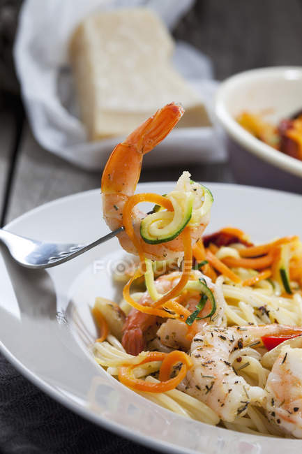 Espaguetis con scampis y verduras en plato, espirales de zanahoria y calabacín, tenedor, primer plano - foto de stock