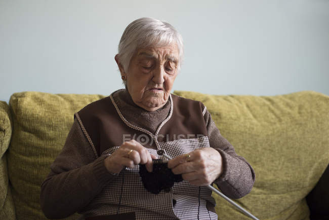Donna anziana che lavora a maglia sul divano a casa — Foto stock