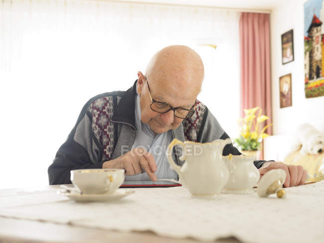 Anciano sentado en la mesa y usando tableta digital - foto de stock