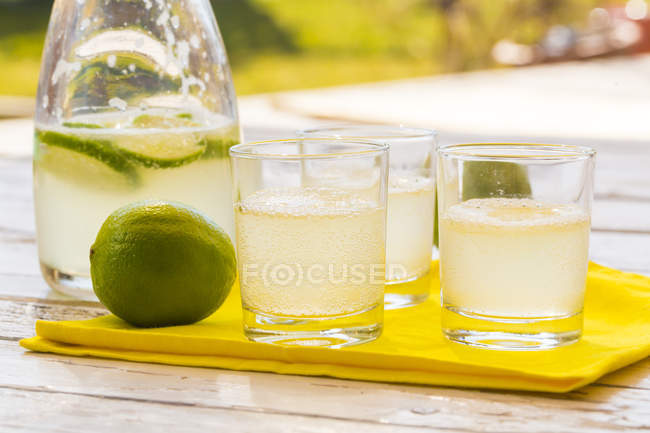 Bicchieri e caraffa di limonata di lime fatta in casa su tessuto giallo — Foto stock