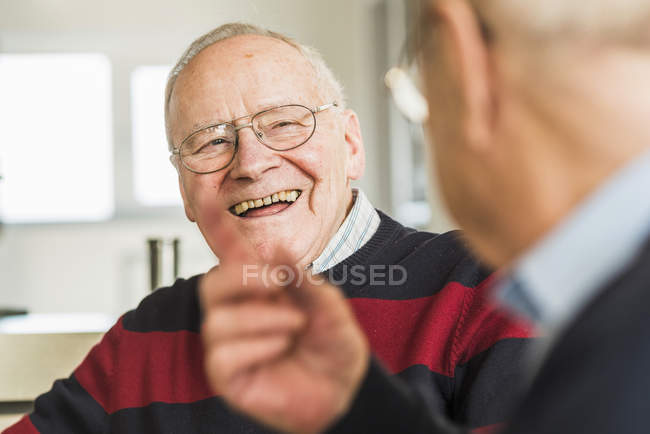 Dos amigos mayores sonrientes hablando en casa - foto de stock