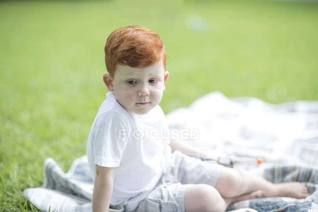 Garçon roux assis sur une couverture de pique-nique — Photo de stock