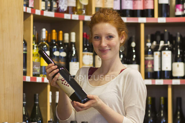 Portrait of smiling young woman in wholefood shop holding wine bottle — Stock Photo