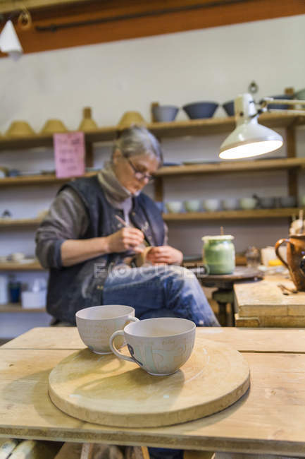 Potier en atelier avec tasses au premier plan — Photo de stock