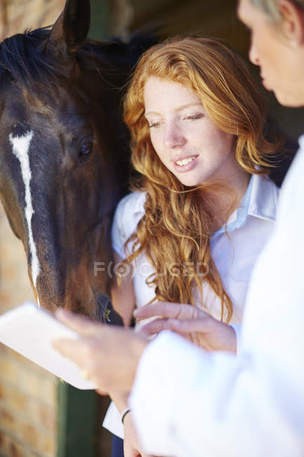 Veterinario con tablet digitale che parla con una giovane donna nella stalla — Foto stock