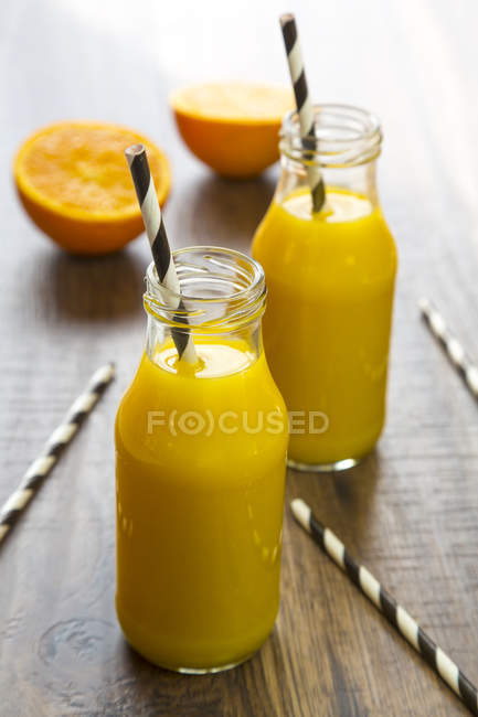 Frullato di arancia in bottiglie di vetro, cannucce su legno — Foto stock