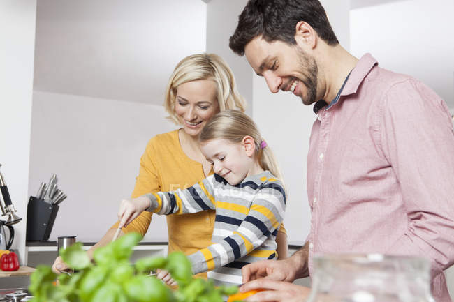 Madre, padre e hija cocinando en la cocina - foto de stock
