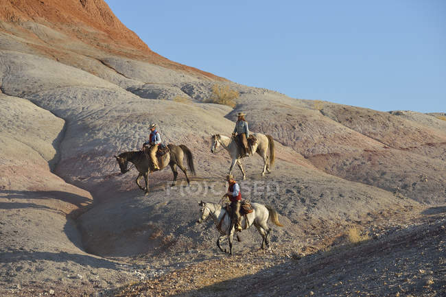 USA, Wyoming, two cowgirls and a cowboy riding in badlands — Stock Photo