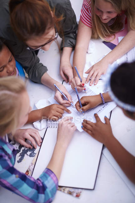 Teacher and schoolgirls writing on paper together — Stock Photo