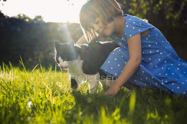 Petite fille avec chat sur une prairie au contre-jour — Photo de stock