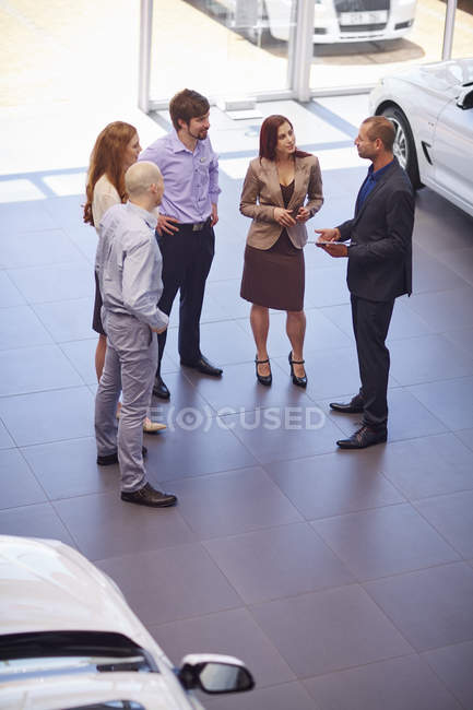 Car dealer meeting with clients in showroom — Stock Photo