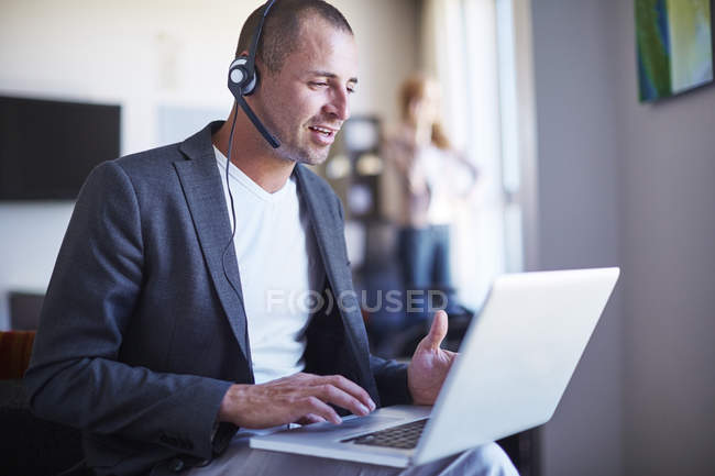 Businessman with headset using laptop in hotel room — Stock Photo