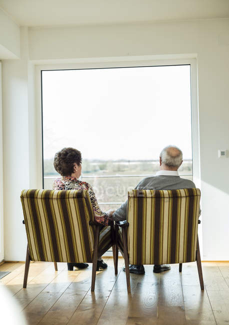 Coppia di anziani seduti fianco a fianco in poltrone guardando attraverso la finestra — Foto stock