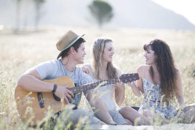 Friends playing guitar while sitting in field — Stock Photo