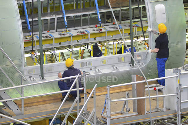 Airplane construction in hangar and workers in safety helmets — Stock Photo