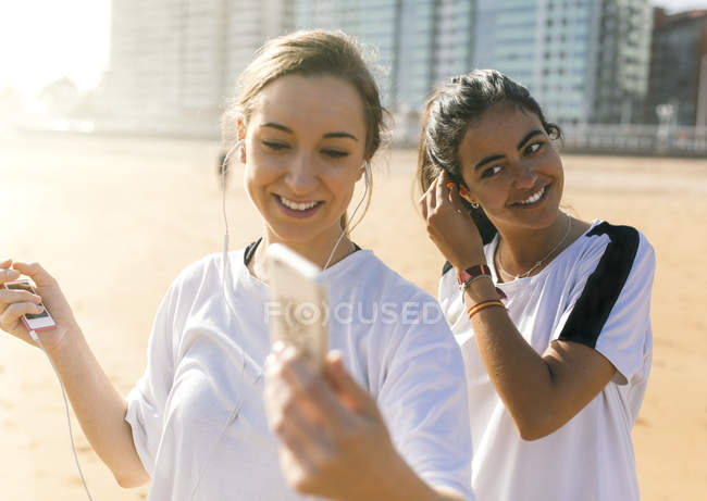 Due giovani donne sportive con auricolari sulla spiaggia — Foto stock