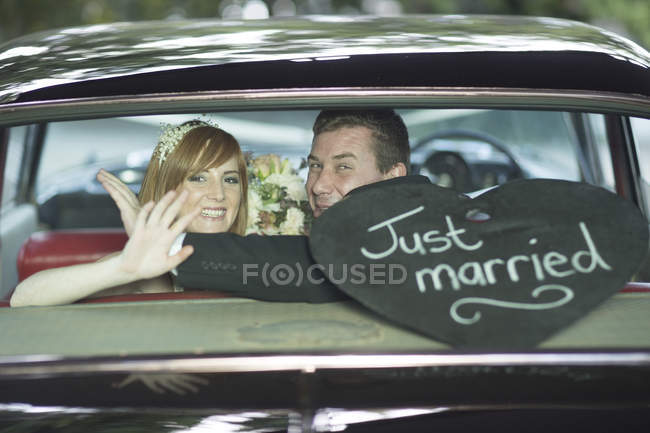 Mariée heureuse et marié agitant dans la voiture après le mariage — Photo de stock