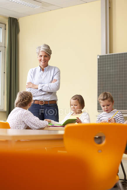 Portrait of smiling Teacher standing with pupils in classroom — Stock Photo