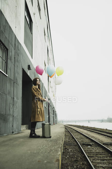 Giovane donna con valigia che tiene mazzo di palloncini sulla piattaforma — Foto stock