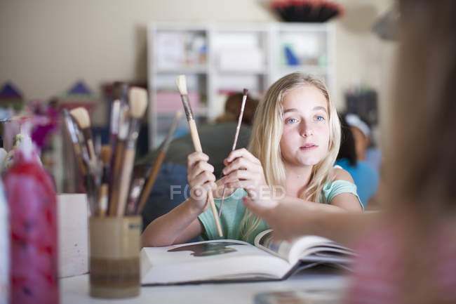 Girl in arts class holding brushes — Stock Photo