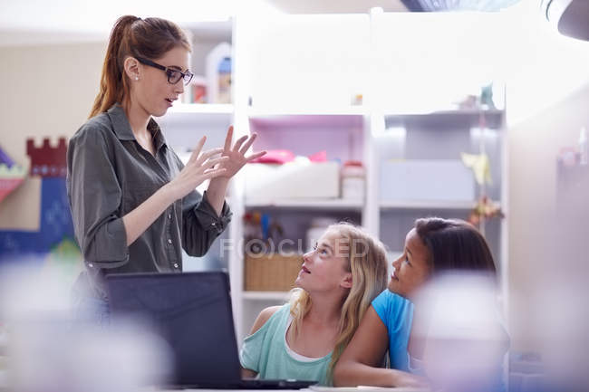 Schoolgirls with laptop looking at gesturing teacher — Stock Photo