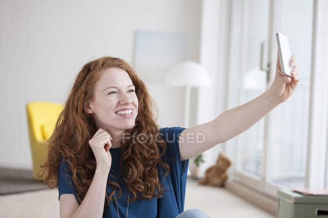 Молода жінка, що сидить у своїй вітальні, беручи selfie зі смартфона — стокове фото
