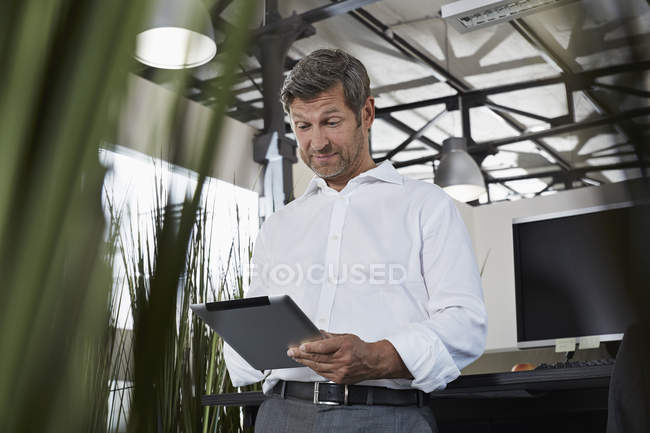 Überraschter Geschäftsmann im Büro schaut auf digitales Tablet — Stockfoto