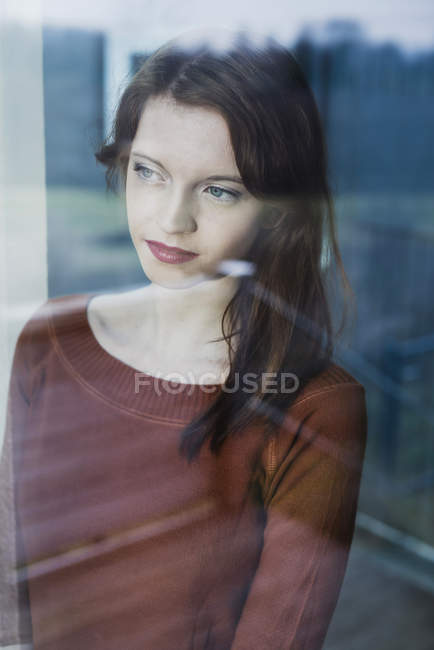 Mujer joven detrás del cristal de ventana - foto de stock