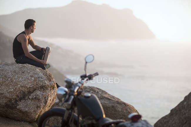 Sudáfrica, Ciudad del Cabo, motociclista sentado en la roca en la costa disfrutando de la vista - foto de stock