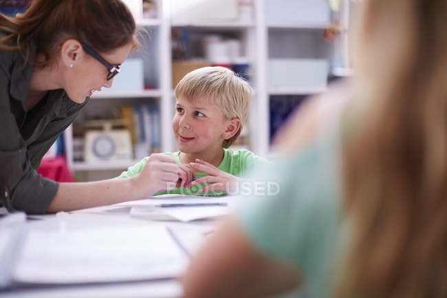 Teacher talking to smiling schoolboy in classroom — Stock Photo