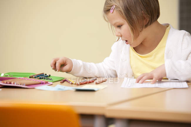 Schoolgirl at school desk with color pencils — Stock Photo