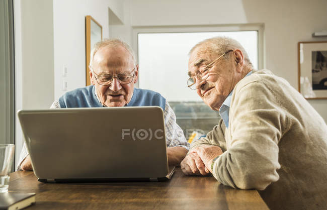 Due amici anziani che utilizzano il computer portatile al tavolo di legno — Foto stock