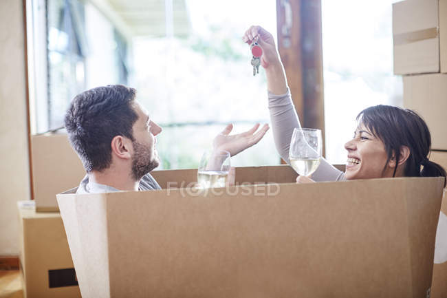 Couple moving house sitting in a box with key and wine glasses — moving