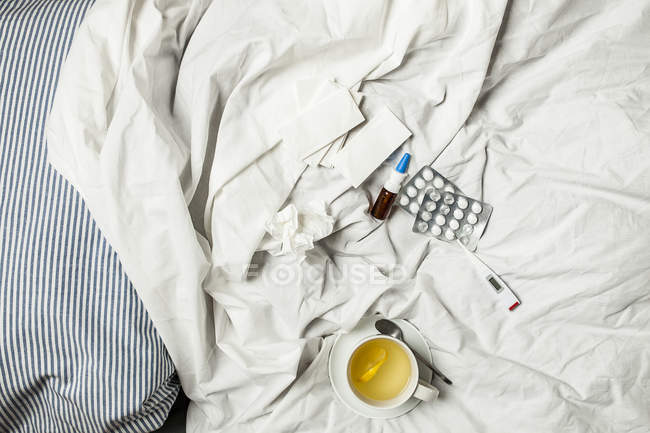 Infusión de limón, termómetro, pastillas, aerosol nasal y tejidos en la cama - foto de stock