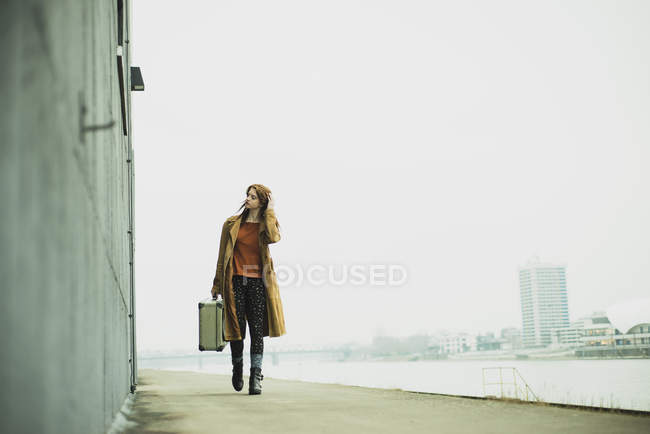 Mujer joven con maleta caminando a orillas del río - foto de stock