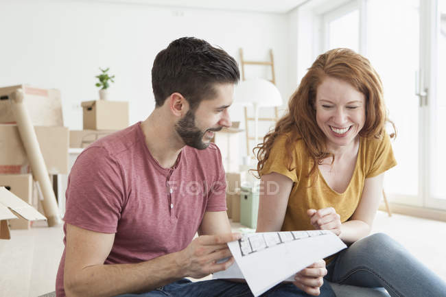 Young couple in new flat with cardboard boxes looking at ground plan — Stock Photo