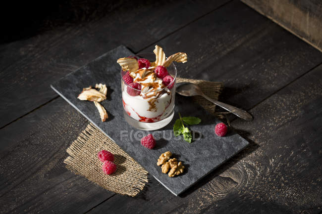 Десерт в стакане с малиной, творогом, йогуртом, сушеным яблоком, миндальными кусочками и шоколадным соусом — стоковое фото