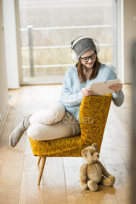 Mujer joven sonriente sentada en silla con tableta digital y auriculares - foto de stock
