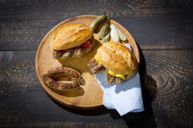 Нюрнбергские сосиски на гриле, пшеничный рулет с горчичным кетчупом и огурцом на деревянной тарелке — стоковое фото