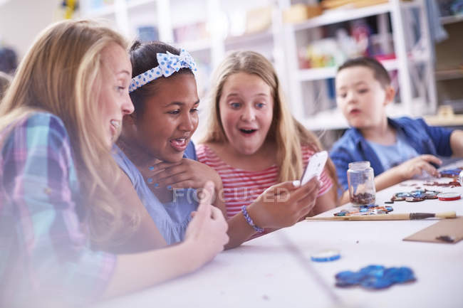 Amazed girls in arts class looking at cellphone — Stock Photo