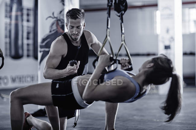 Тренер по фитнесу проводит время с женщиной, занимающейся подтягиванием — стоковое фото