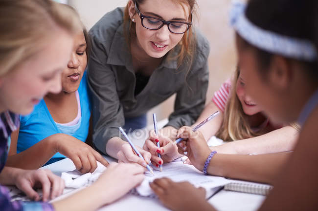 Teacher and schoolgirls writing on paper together — Stock Photo
