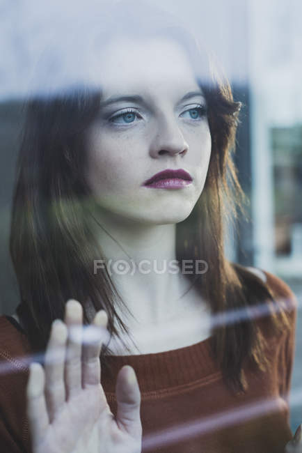 Mujer joven seria detrás del cristal de la ventana - foto de stock