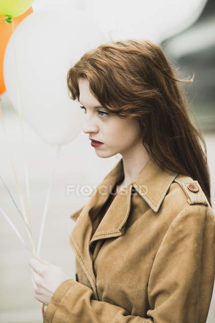Mujer joven con abrigo sosteniendo un montón de globos - foto de stock