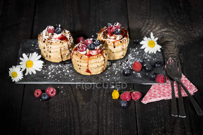 Filo pastry tartlets filled with vanilla ice cream and whipped cream garnished with blueberries and raspberries on slate — Stock Photo