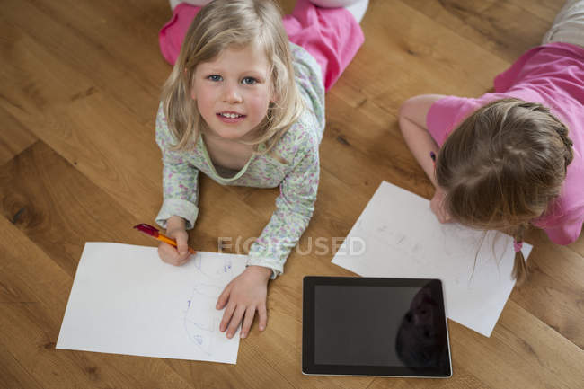 Due sorelle con tablet digitale e fogli di carta sul pavimento — Foto stock