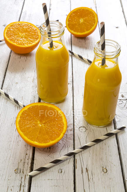 Orange smoothie in glass bottles, straws on wood — Stock Photo